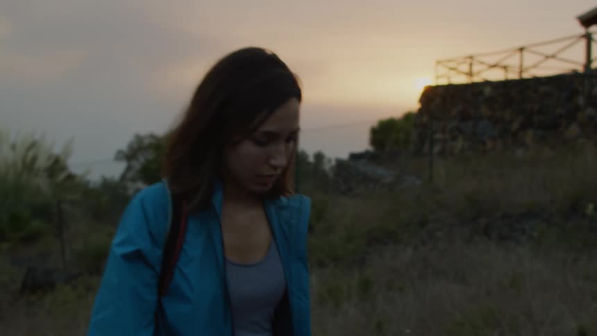A woman repeatedly glances behind her while walking outdoors in the evening