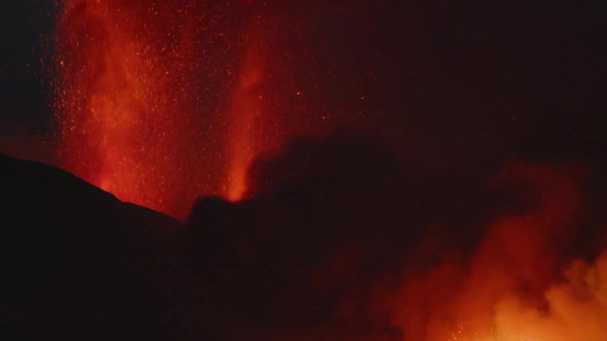 Molten lava sprays into the air from an erupting volcano as smoke billows into the night sky
