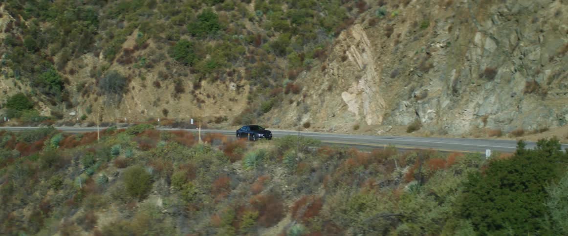 A dark blue car traveling on a mountain road