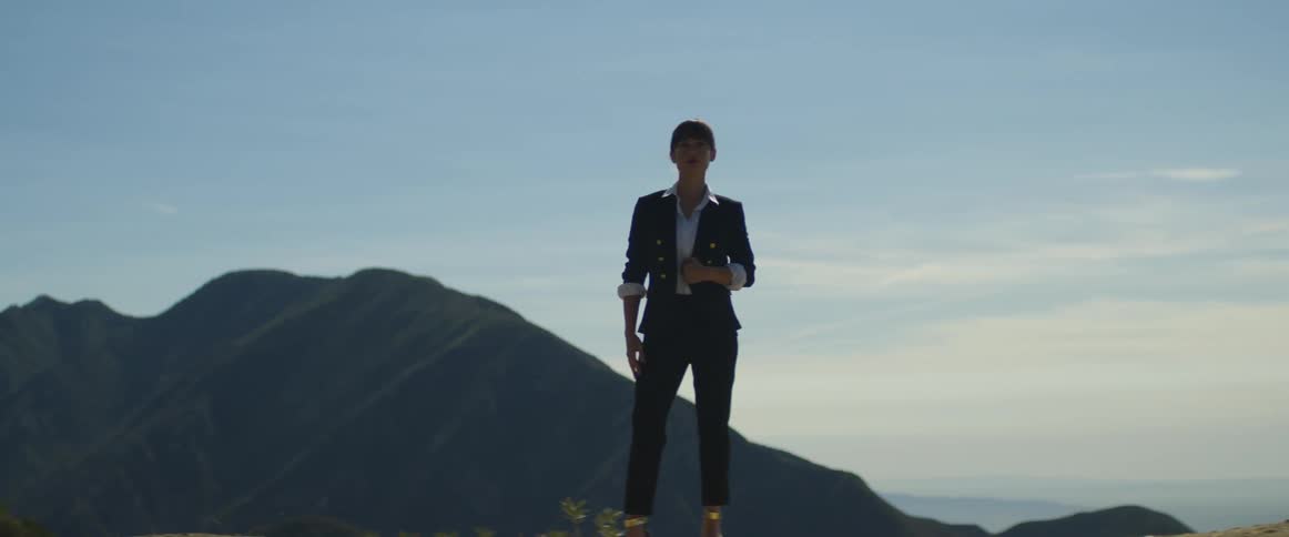 A woman wearing fashionable clothing poses in the mountains during the day