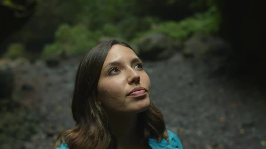 A woman is standing in a clearing in a forest and looking up