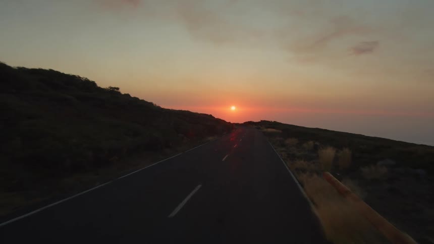 The sun sits low in the sky above a long and lonely road near the ocean