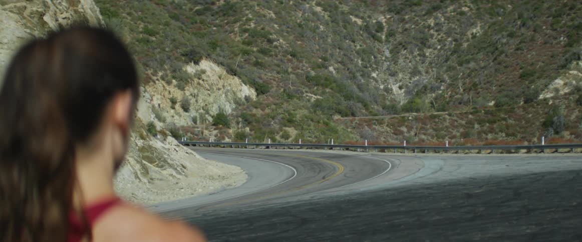 Woman waits near the road by the mountains as a car approaches on the highway