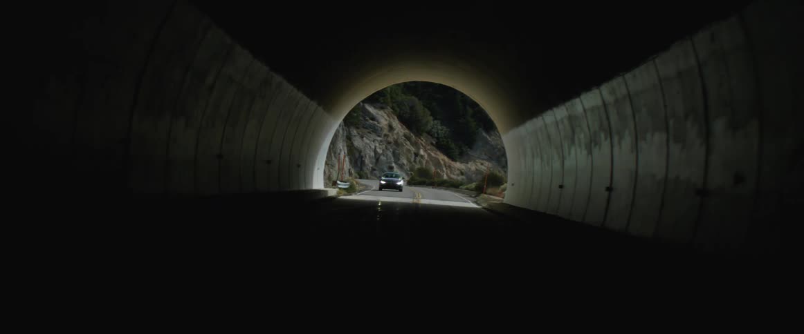 A car driving through the mountains enters a dark tunnel