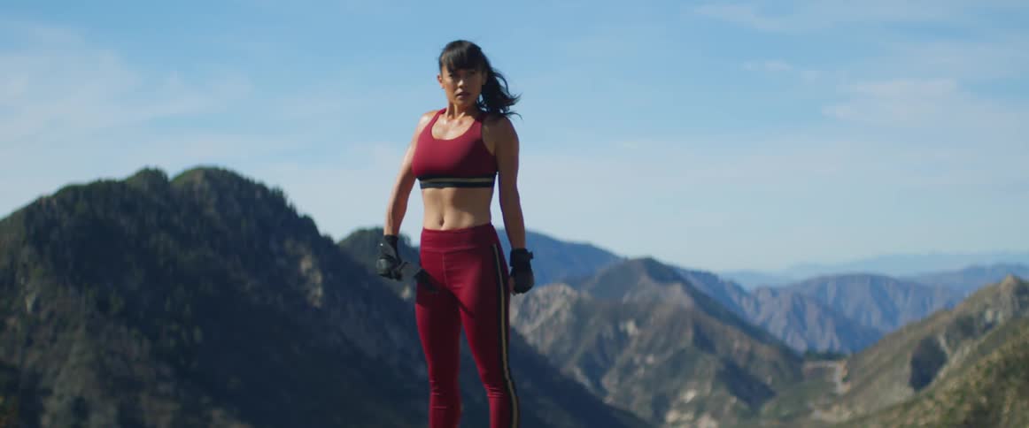 A woman is standing on a ridge of a valley with mountains in the background