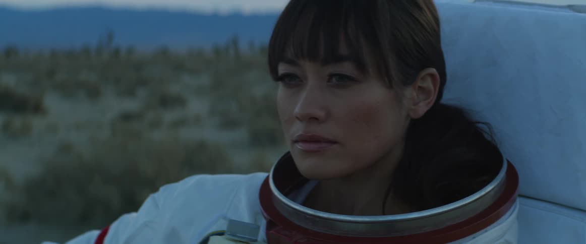 A woman in full makeup standing in the desert wearing an astronaut space suit with pack