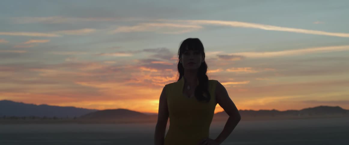A woman stands on the shore as the sun sets and looks off in to the distance