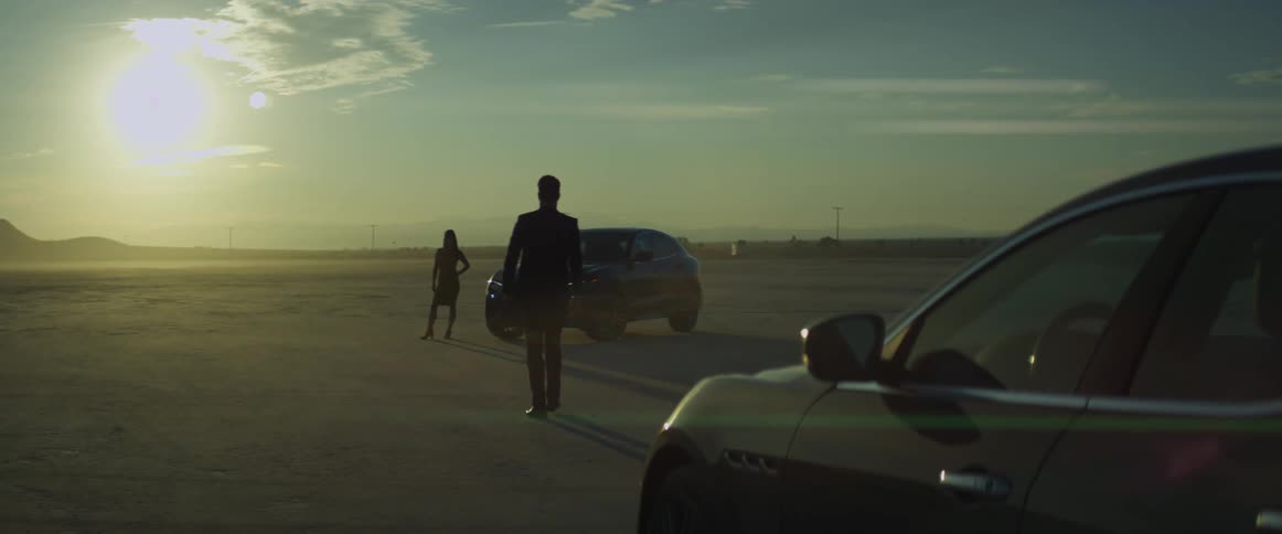 Silhouette of a man and a woman meeting in the desert close to parked cars at sunset