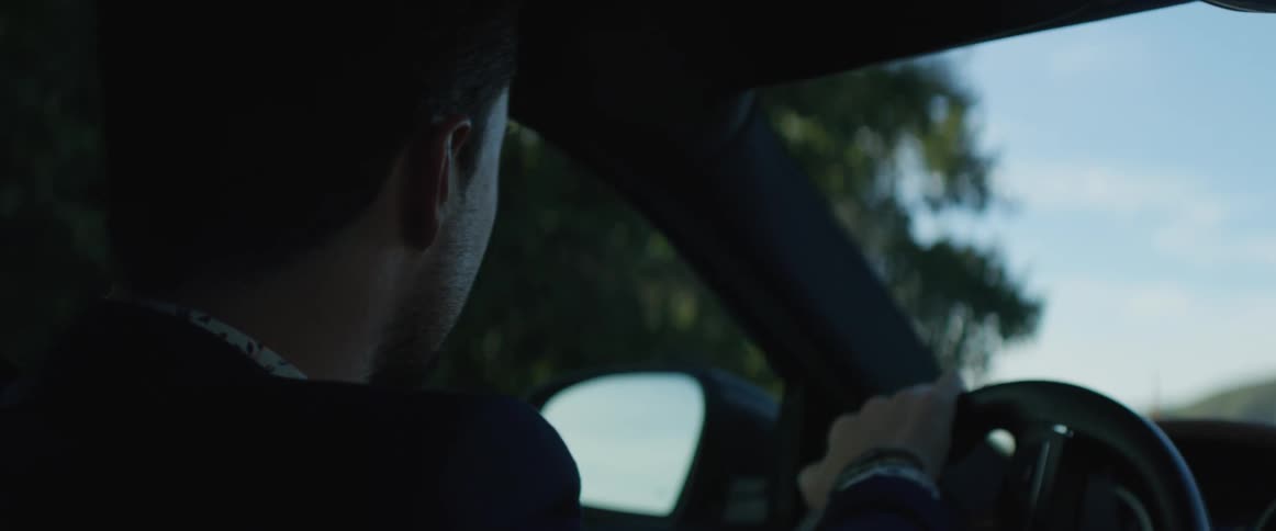A man looks around through the windshield as he drives on a mountain road