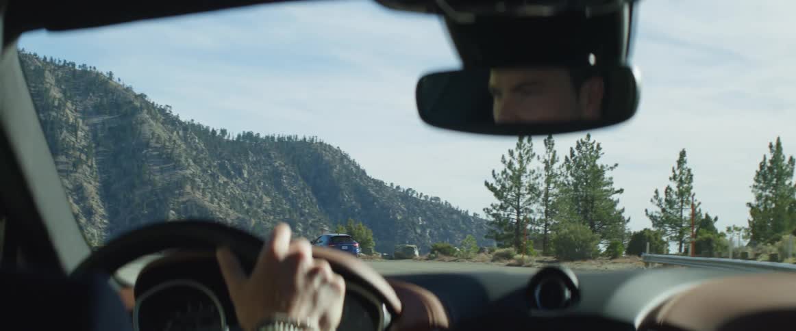 Man driving a car follows another car on a highway near the mountains