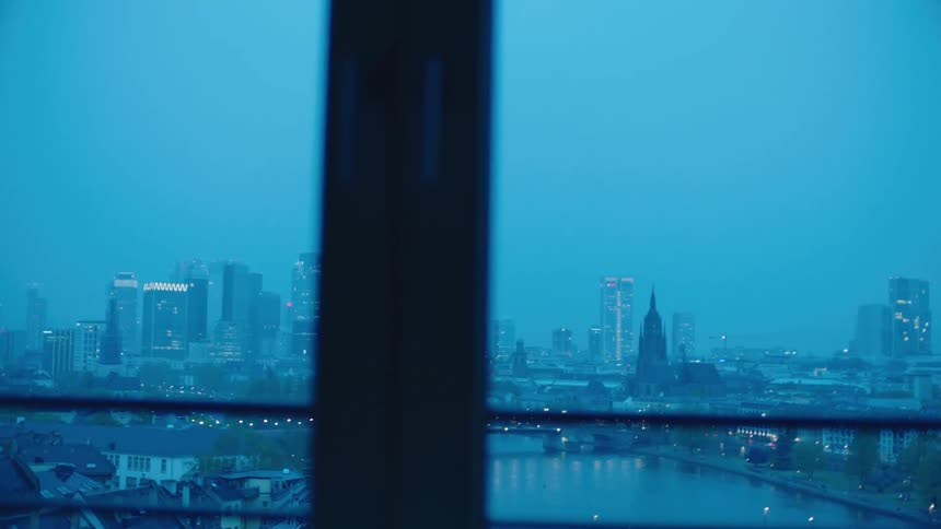 Woman with bun holding cup is silhouetted against the city skyline at apartment building at dusk