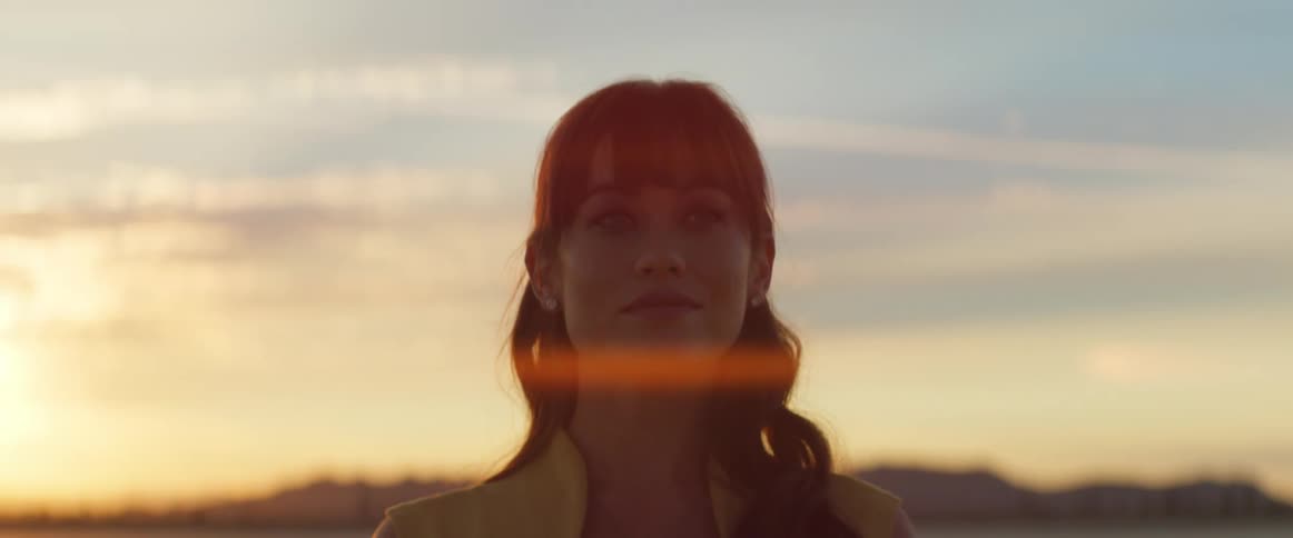 A woman standing and smiling as the sun glares and shines as it sets