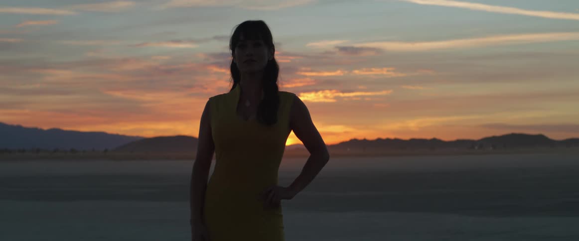 A woman is standing outdoors while the sun is setting