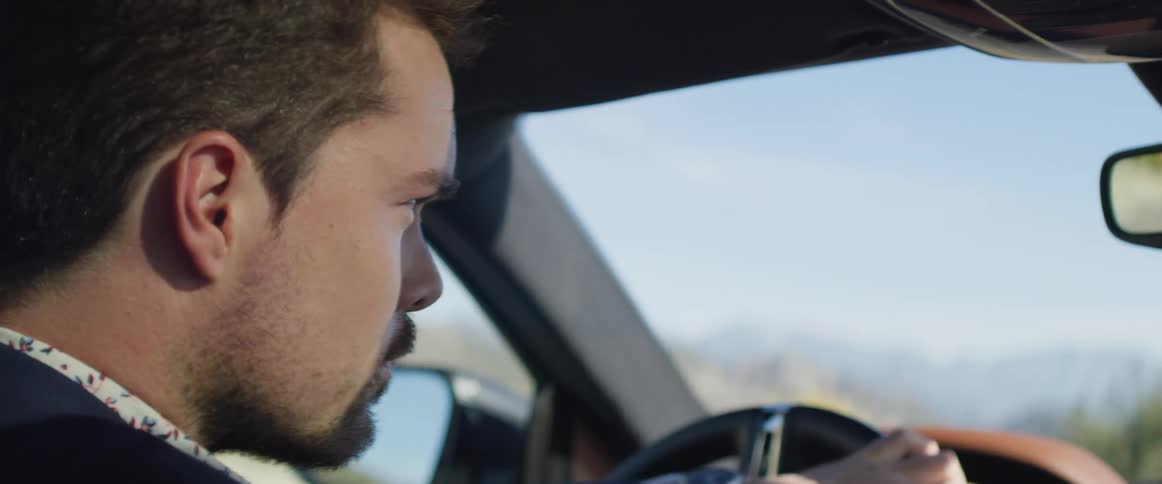 Man with goatee and blazer jacket drives car on road