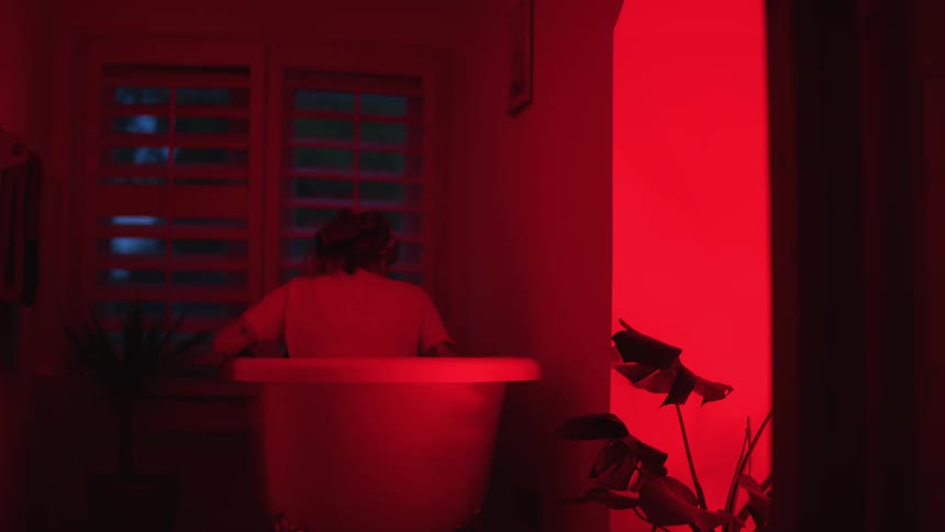 A young woman is sitting in her bathtub at night time