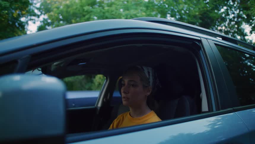 A woman sits in her car in a parking lot