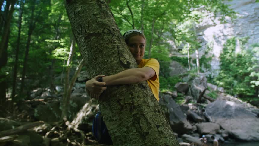 A woman smiles and kisses the tree she is hugging