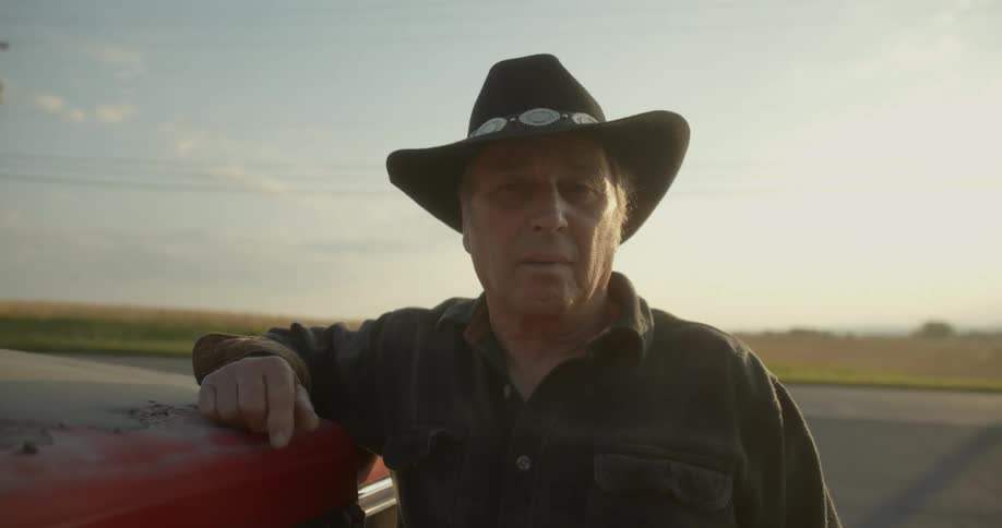 A man is standing on the side of a road leaning on the hood of his truck