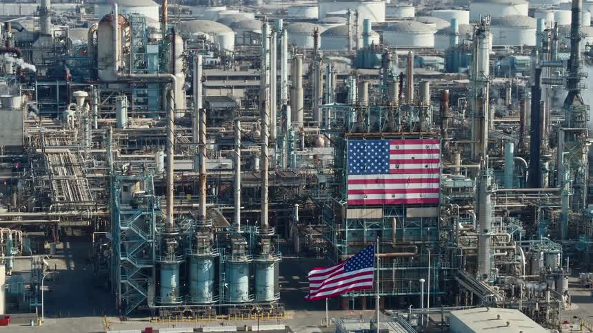 Large american flags fly and hang outside a refinery