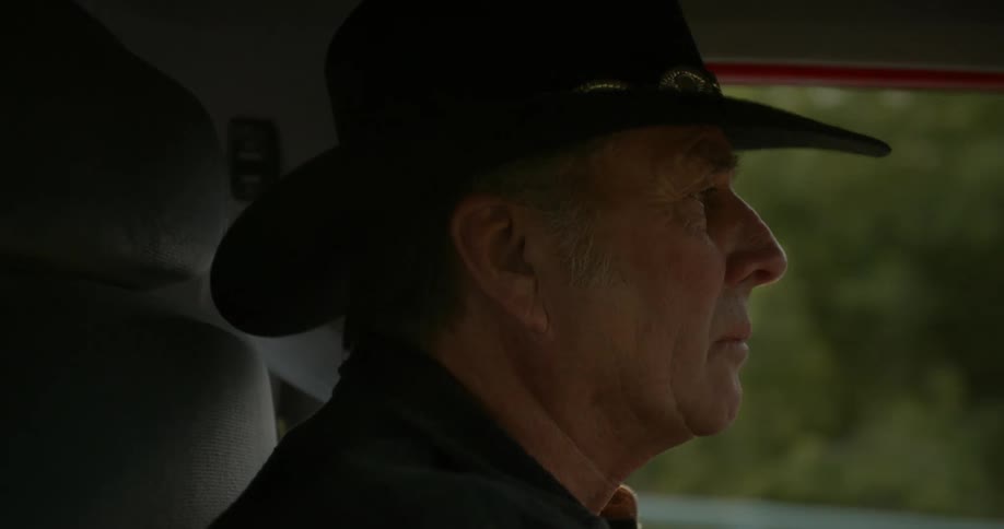 An elderly white man is driving his car in the middle of the day