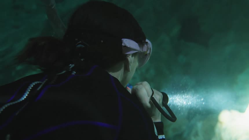 A woman shines a flashlight on the bottom while cave diving