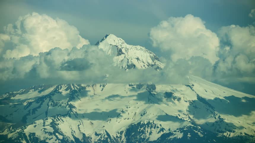 Mount Hood tight aerial shot covered in a lot of snow with puffy white clouds around it