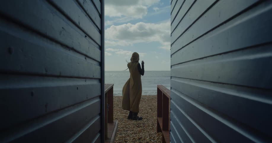 A woman walks between beach huts and looks out to sea