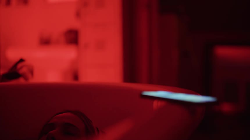A woman sinks down in her bathtub and sets down her smartphone