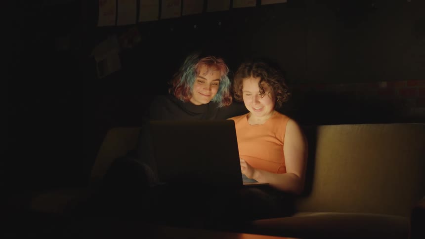 Two people talk while looking at a laptop