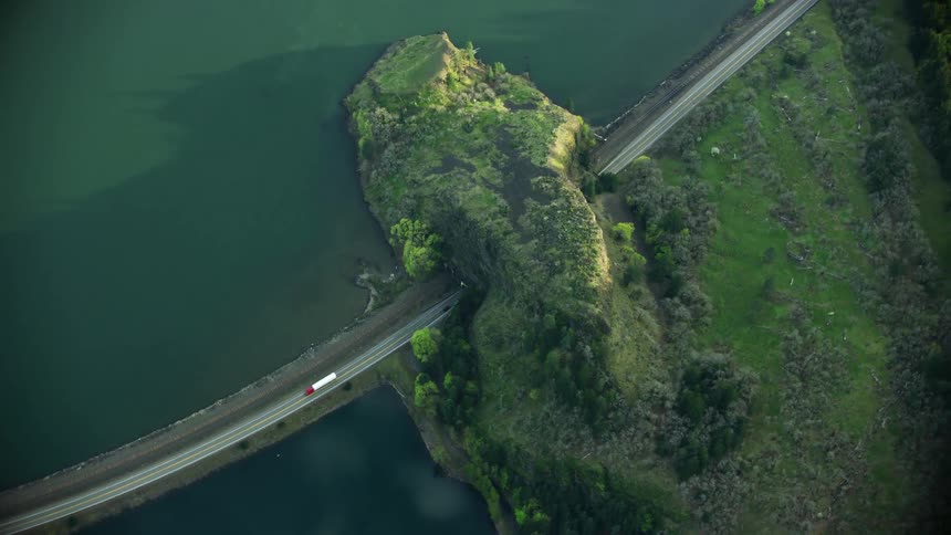 Aerial Long haul Semi Truck drives through a tunnel next to a river and lake in a stunning look down aerial from high above