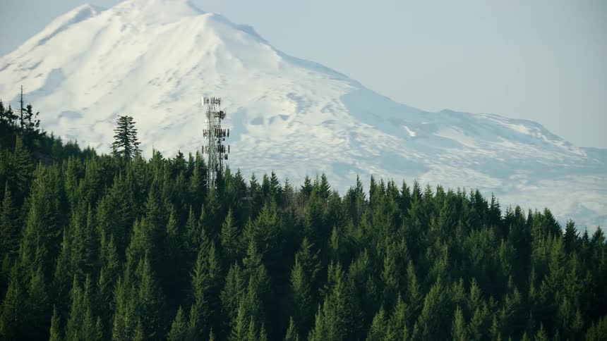 Several Cell phone transmission towers stand in front of a massive mountain as the aerial camera rapidly rotates around them