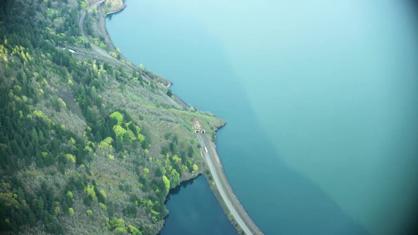 A semi truck drives down a narrow road along the coast before passing through a tunnel as American truckers keep American goods moving and in business