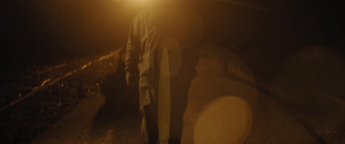 Person wearing a hooded jacket is back lit by streetlight at night
