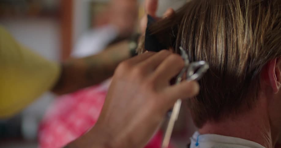 A tattooed barber cutting a male clients hair with scissors