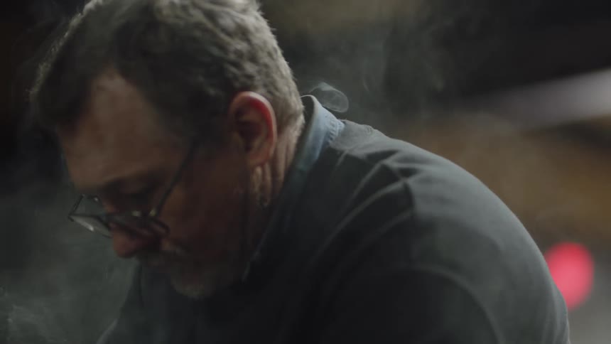 Smoke billows around a man while he stands outside at night