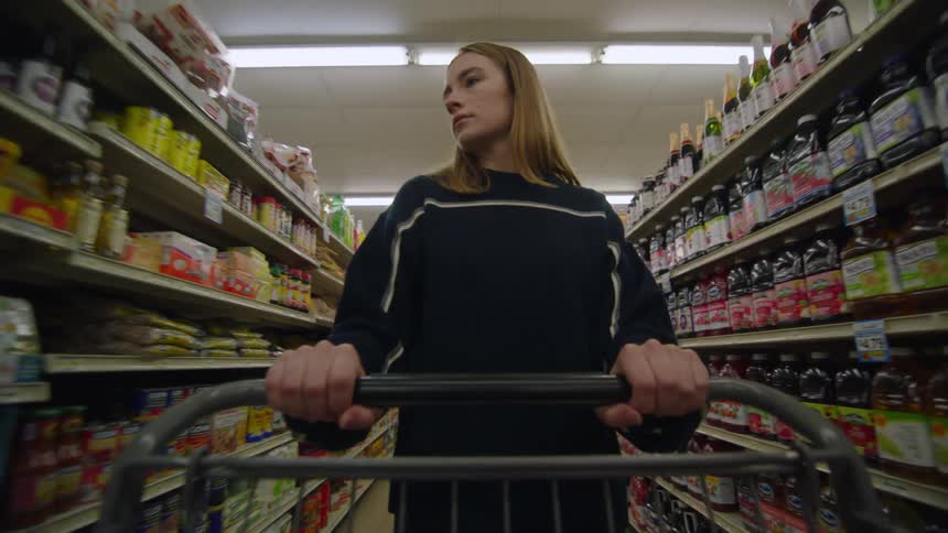 Woman pushes a shopping cart down the store aisle as she looks at the products on the shelves