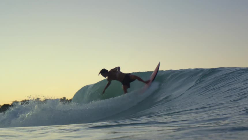 A male surfer riding an ocean wave at sunset