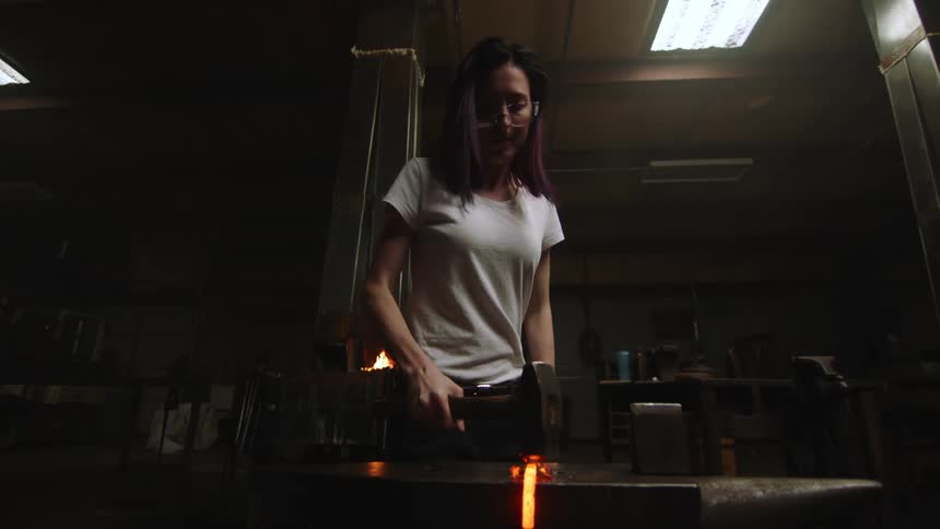 A woman is hammering hot iron