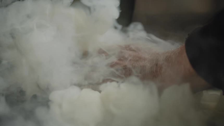 Smoke is rising from a container and a man is placing his hands over the smoke as it rises