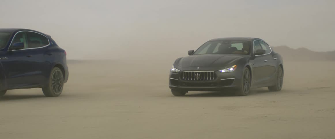 Two automobiles are traveling across a hazy desert and there are mountains in the distance