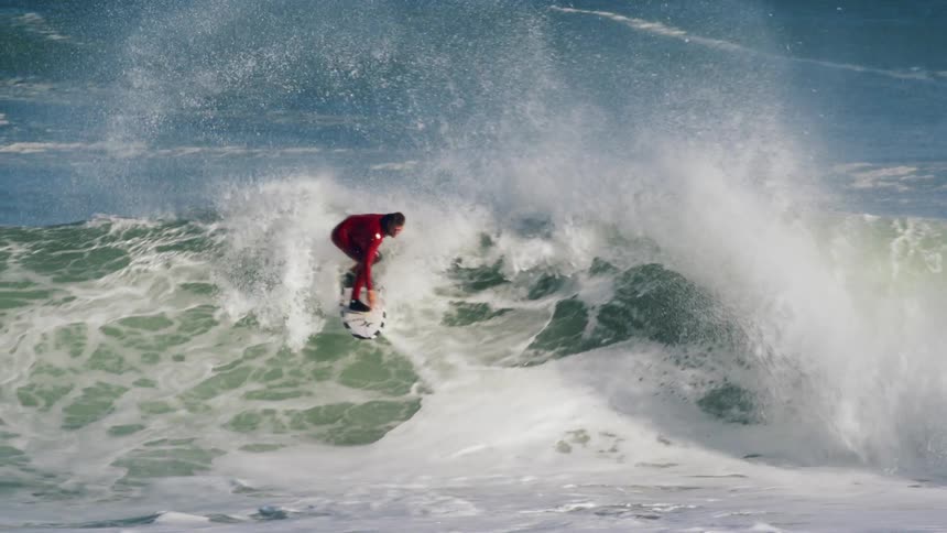 A man wearing a red wetsuit surfs a curling breaking wave