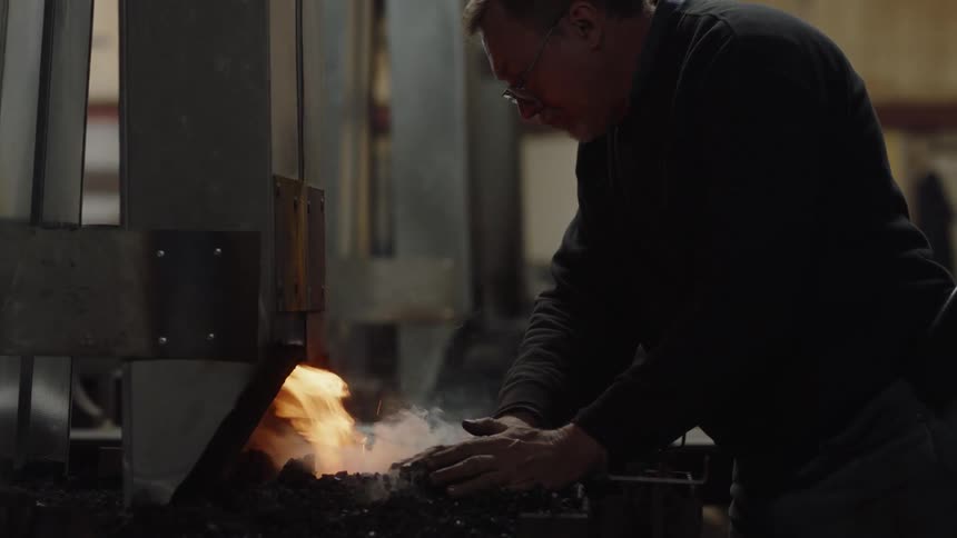 A man using his bare hands to spread and move chips toward a flaming smoking fire