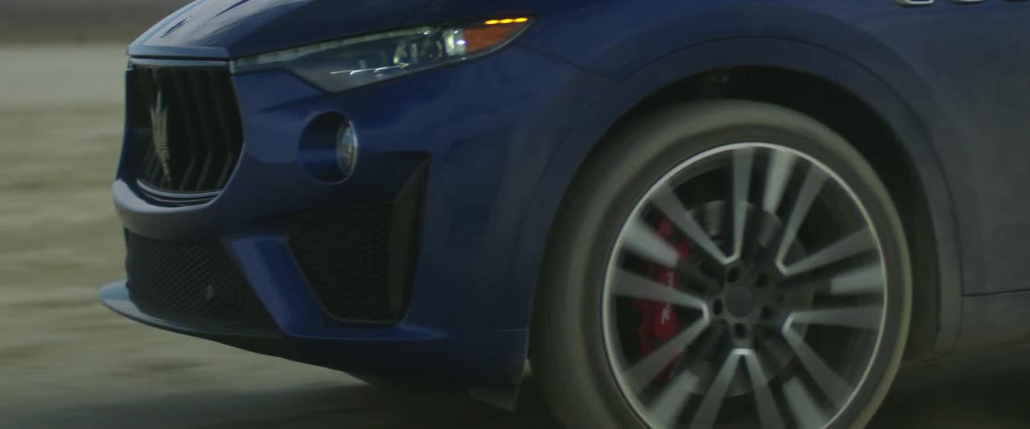 A dark blue automobile travels on a road and the wheels spin as it moves