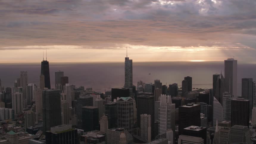 Tall buildings and skyscrapers stand tall in a big city along the coast as the sun shines thought the clouds over the lake