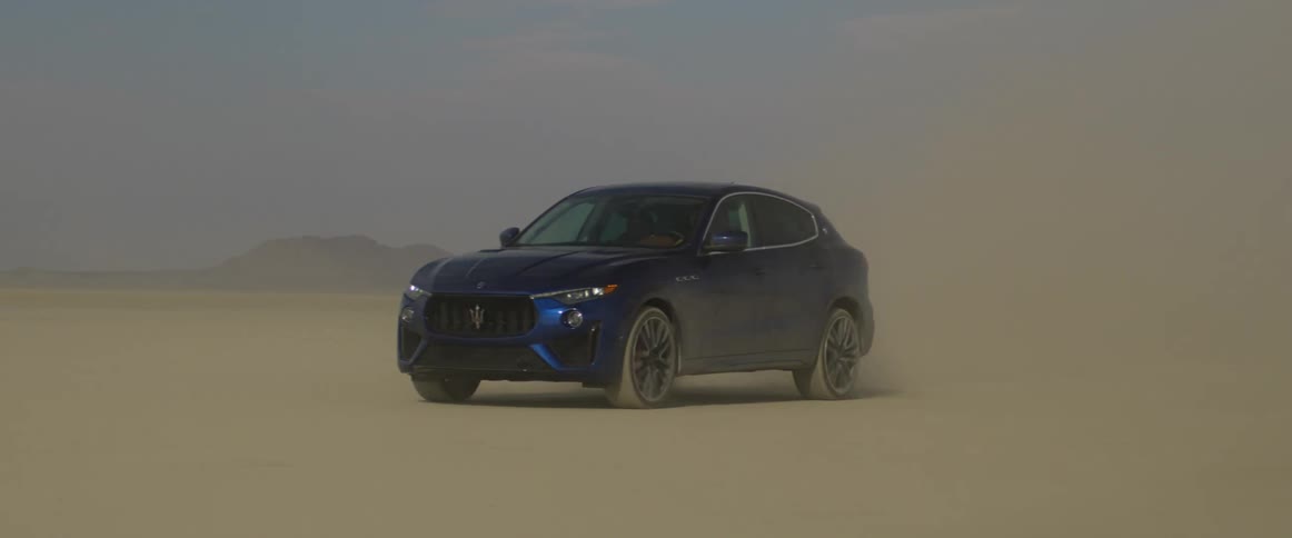 Blue car drives through desert kicking up dust
