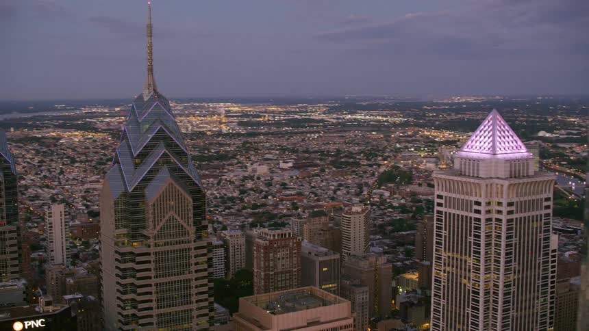Skyscrapers with flashing lights on top stand near the other buildings in the city at dusk