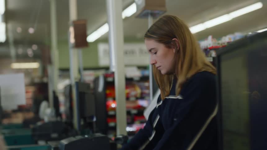 A teenage girl unloads her cart of food at a grocery store