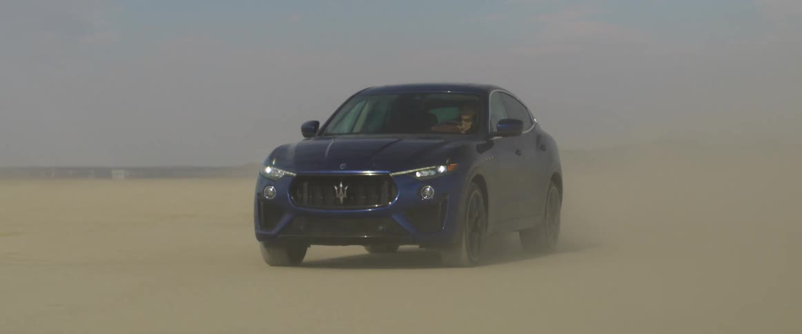 A car is kicking up sand as someone drives it across a desert