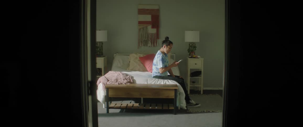 A woman sits on the side of her bed while looking at the screen of her smart phone