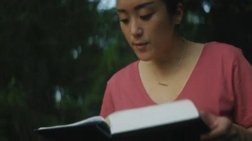 Woman with a bun a necklace a pink blouse and jeans reads book in the forest